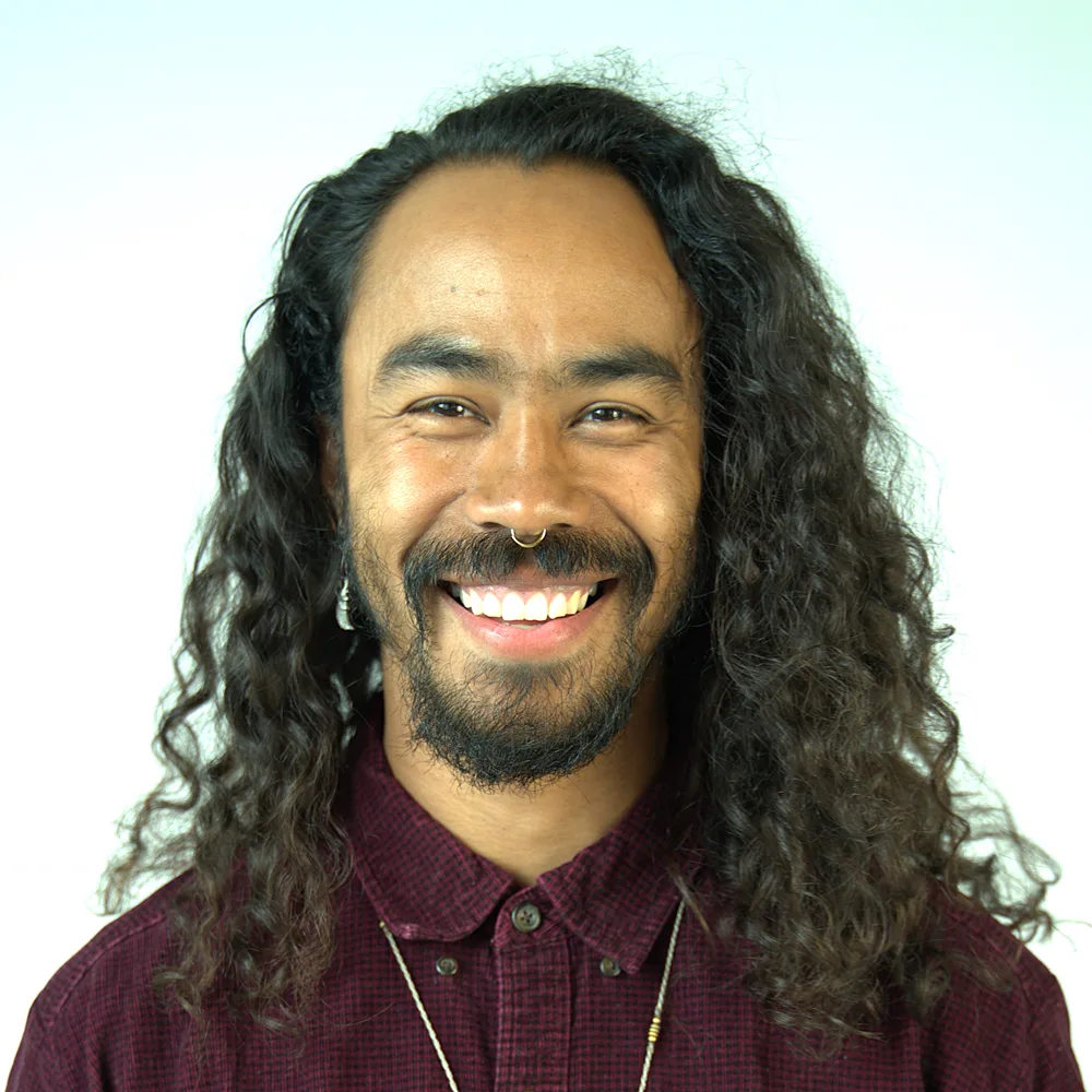 Spencer Z. Pearman, sonriendo, con el pelo largo y rizado y camisa granate.